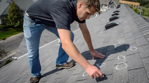 Roofer marking damaged shingles during inspection.