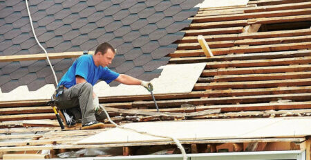 Roofer installing shingles and repairing roof decking.