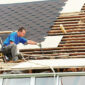 Roofer installing shingles and repairing roof decking.