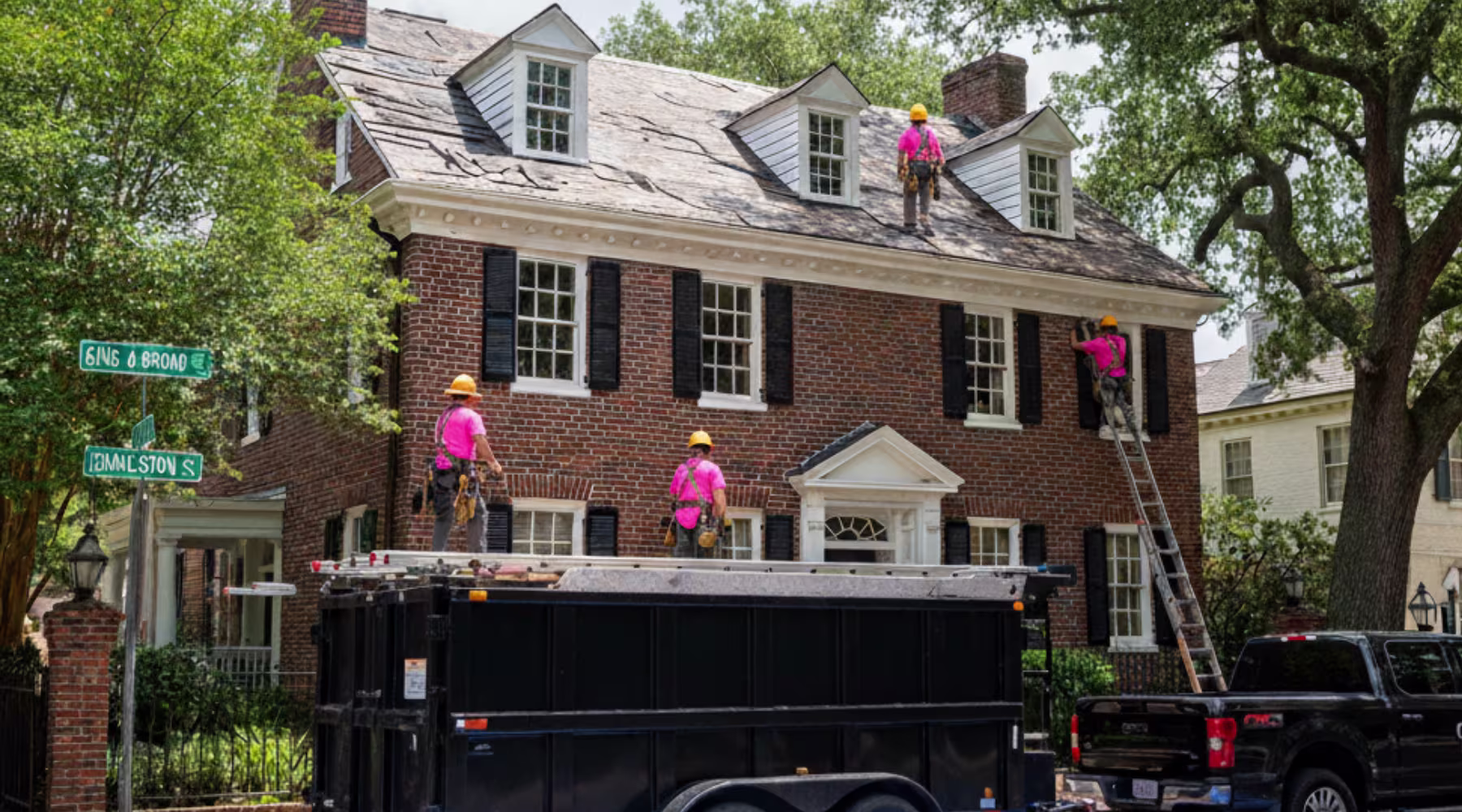 roof replacement contractor Roofing contractors wearing pink shirts and yellow helmets work on replacing the roof of a large brick house at the corner of King & Broad and Pinckney Streets.
