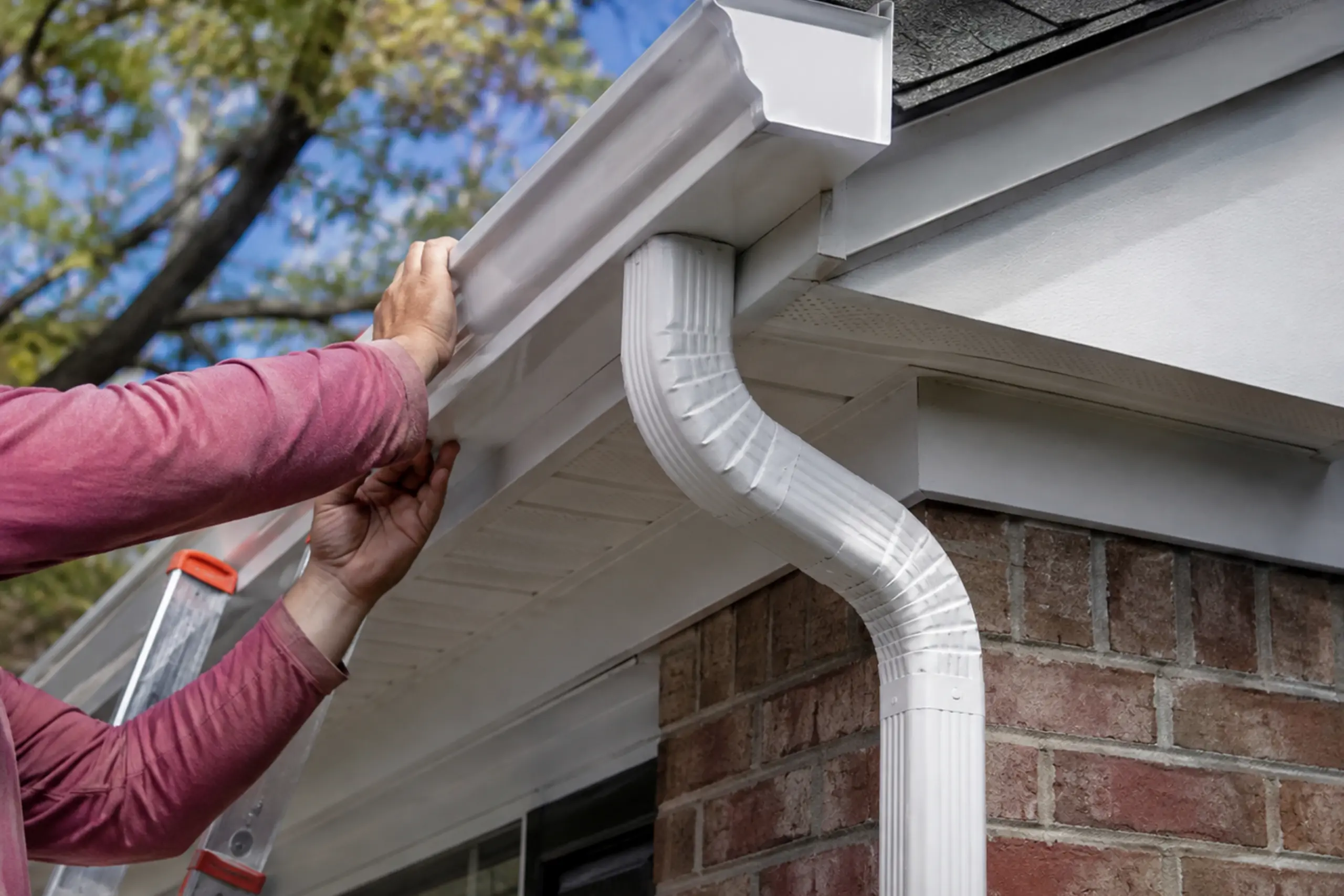 gutter installation of a house Close-up of hands installing a white gutter and downspout on a brick house